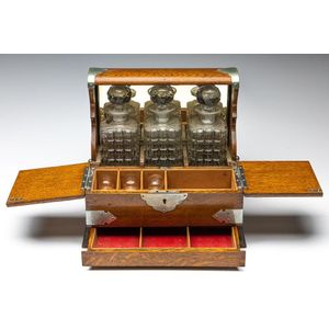 An oak three bottle tantalus with secret drawer, three section…