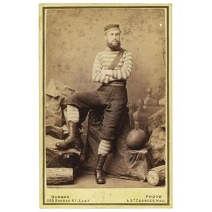 A bearded footballer in full playing outfit with inflated oval…