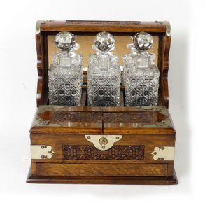 An Edwardian oak three-bottle tantalus, the square section…