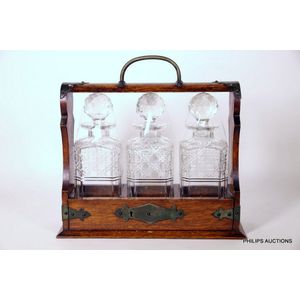 An antique oak tantalus with three cut crystal decanters, 19th…