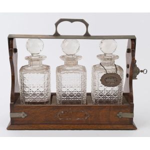 An antique three bottle tantalus with hobnail crystal decanters,…