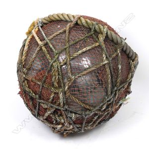 A glass fishing float, bound in fine netting and heavy rope,…