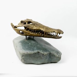 A brass sculpted crocodile skull on a serpentine boulder,…
