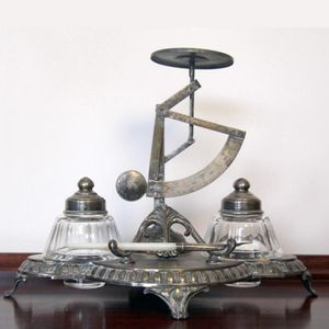 A plated ink stand desk set. Compass flanked by ink bottles on…