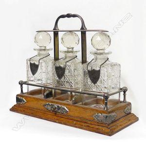 An Edwardian oak three-bottle tantalus, the square section…