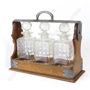An Edwardian oak and silver plate framed three-bottle tantalus,…