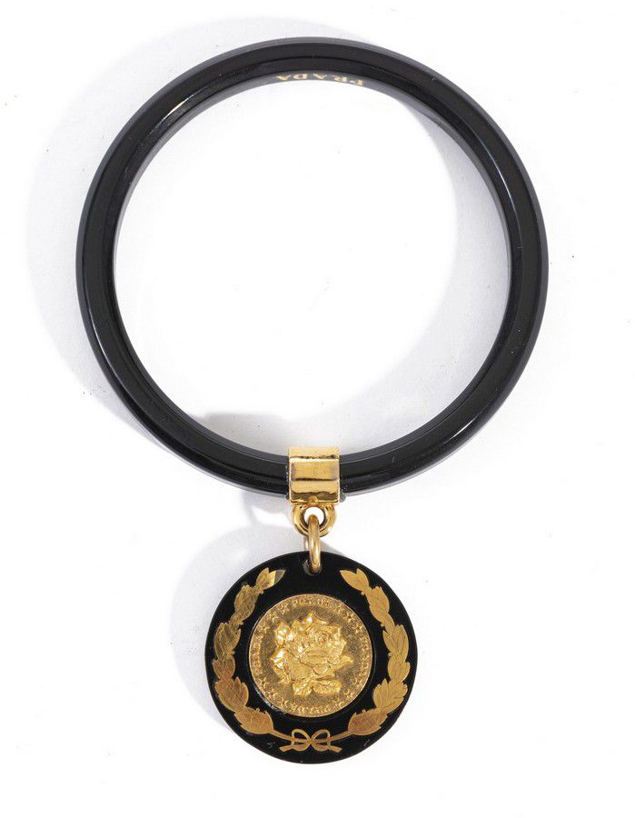 A bangle by Prada, styled in black composite with gold metal